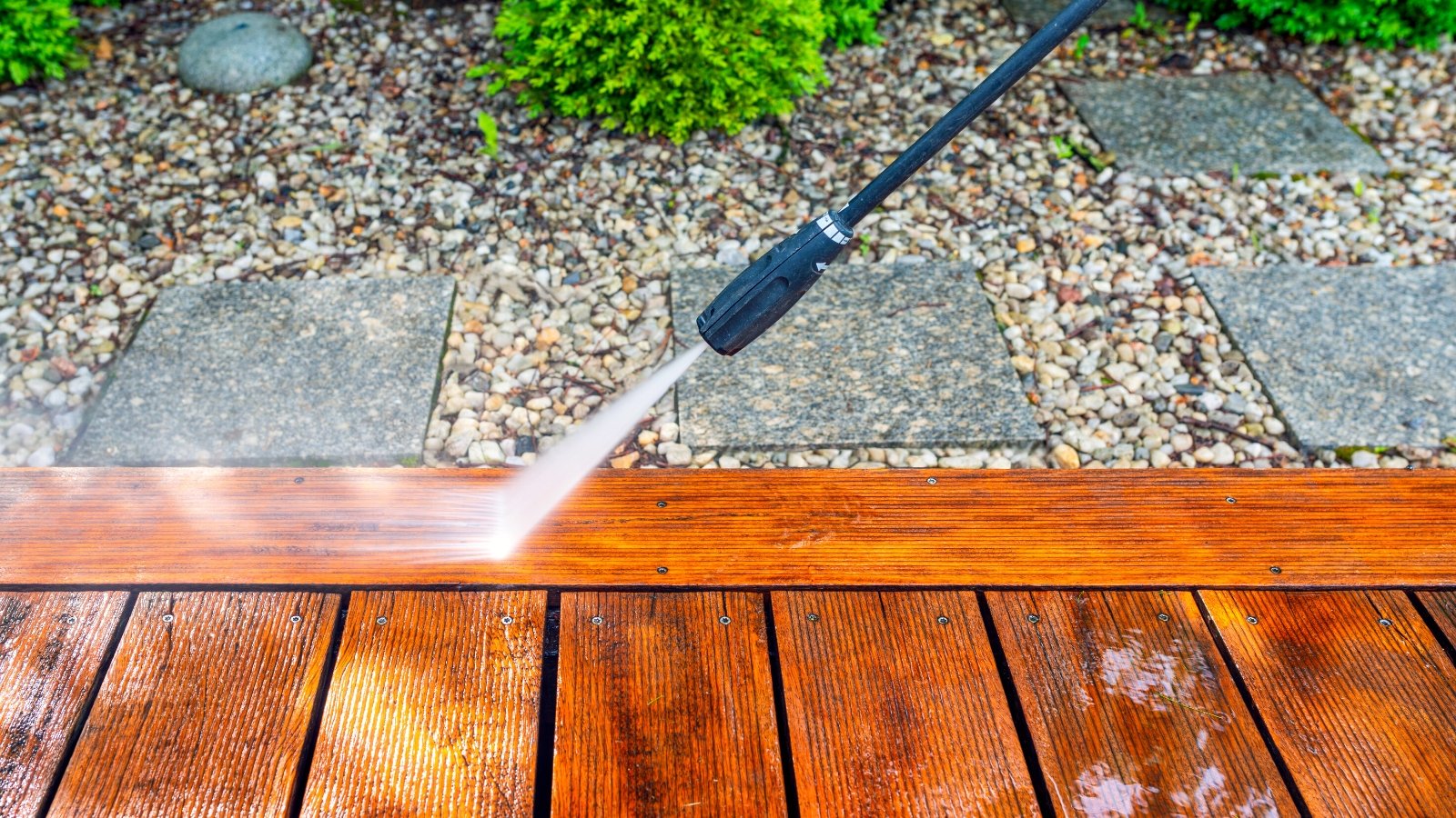 Cleaning the terrace with a power washer. It is characterized by a high-pressure hose and a wand with various interchangeable nozzles. Strong water pressure streams from the pump and cleans the wooden surface on the terrace.