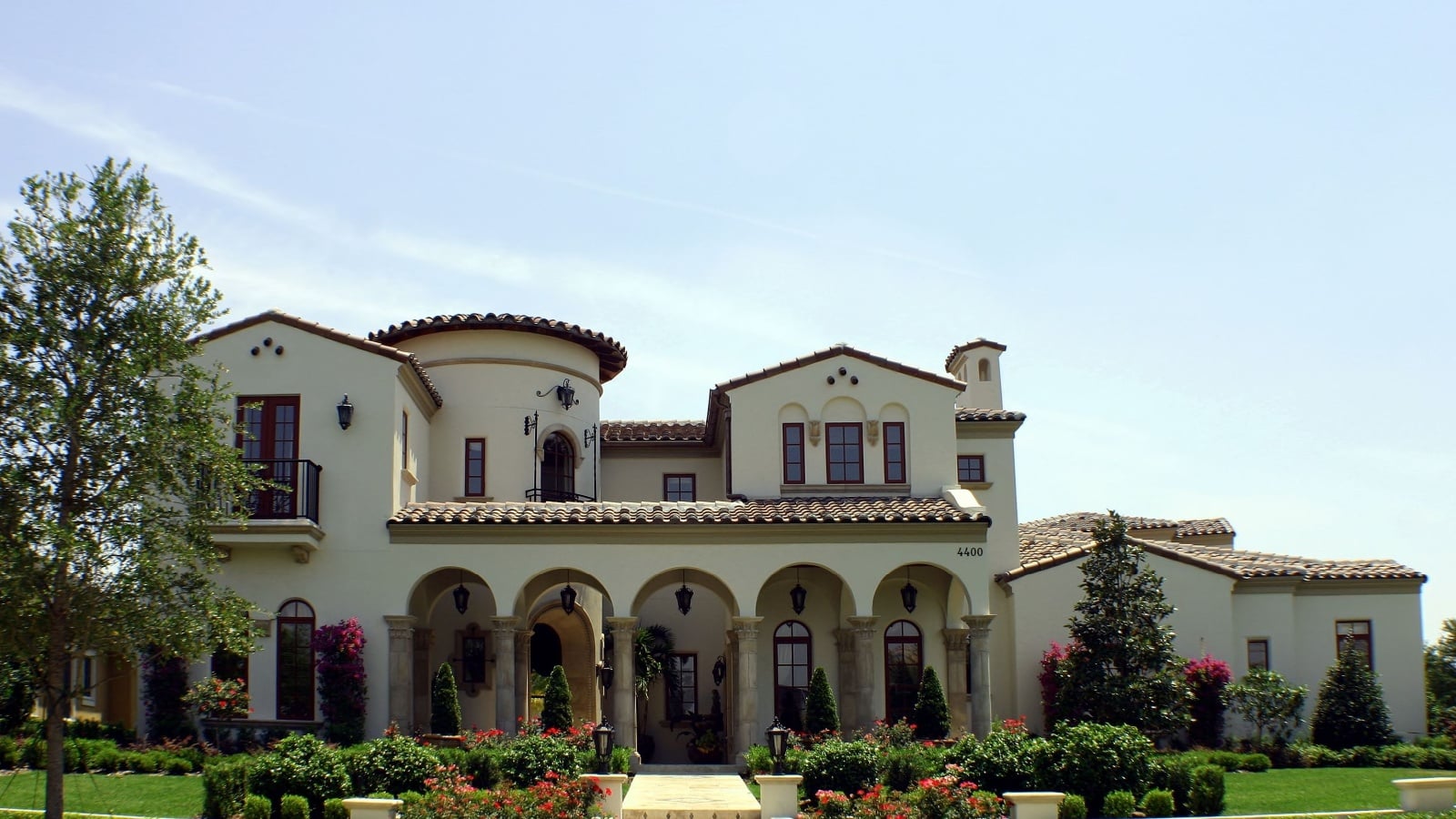 A spanish style home with beautiful gardens on a sunny day.