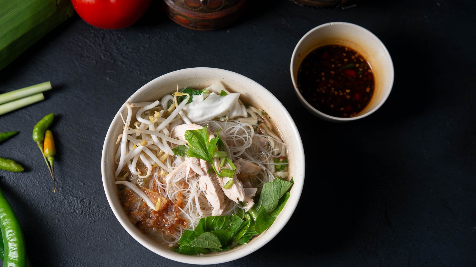 Overhead image of Asian noodle dish with dipping sauce and chilies.