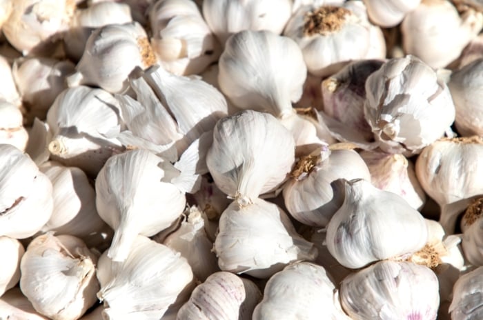 An arrangement of bulbs with papery white skin and individual segments or cloves visible, placed on a wooden surface, showcasing the vegetable’s distinct texture.