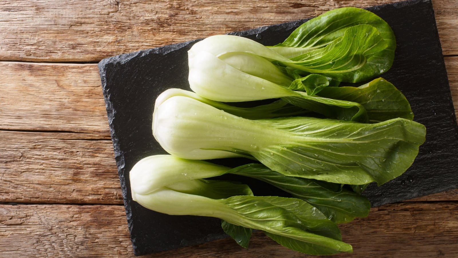 A bunch of small, crisp, light green leafy vegetables with thick white stems, neatly stacked on a wooden surface.