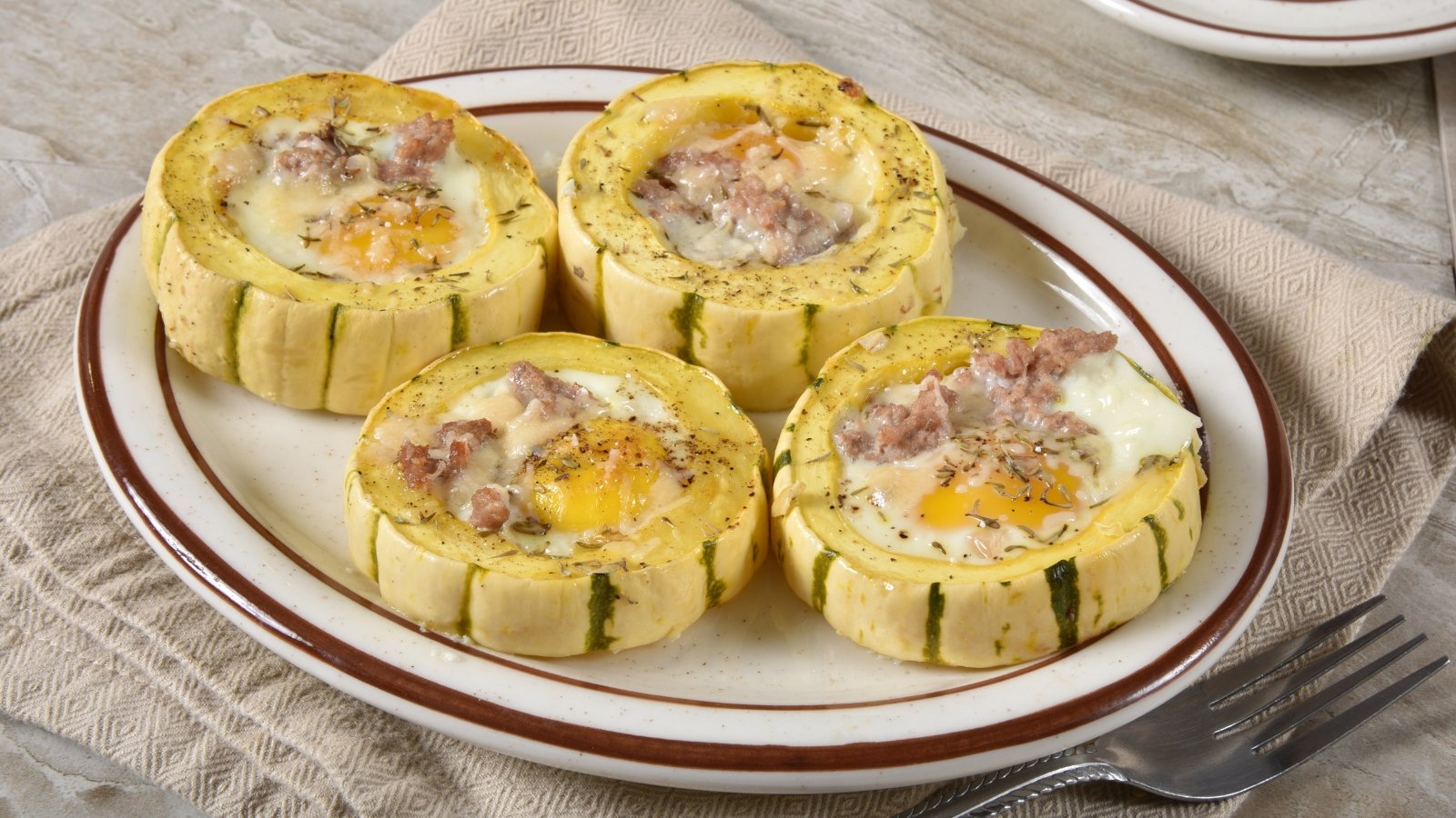Close-up of golden-brown baked squash rounds filled with a creamy egg and tuna mixture, generously topped with melted cheese, served on a white plate.