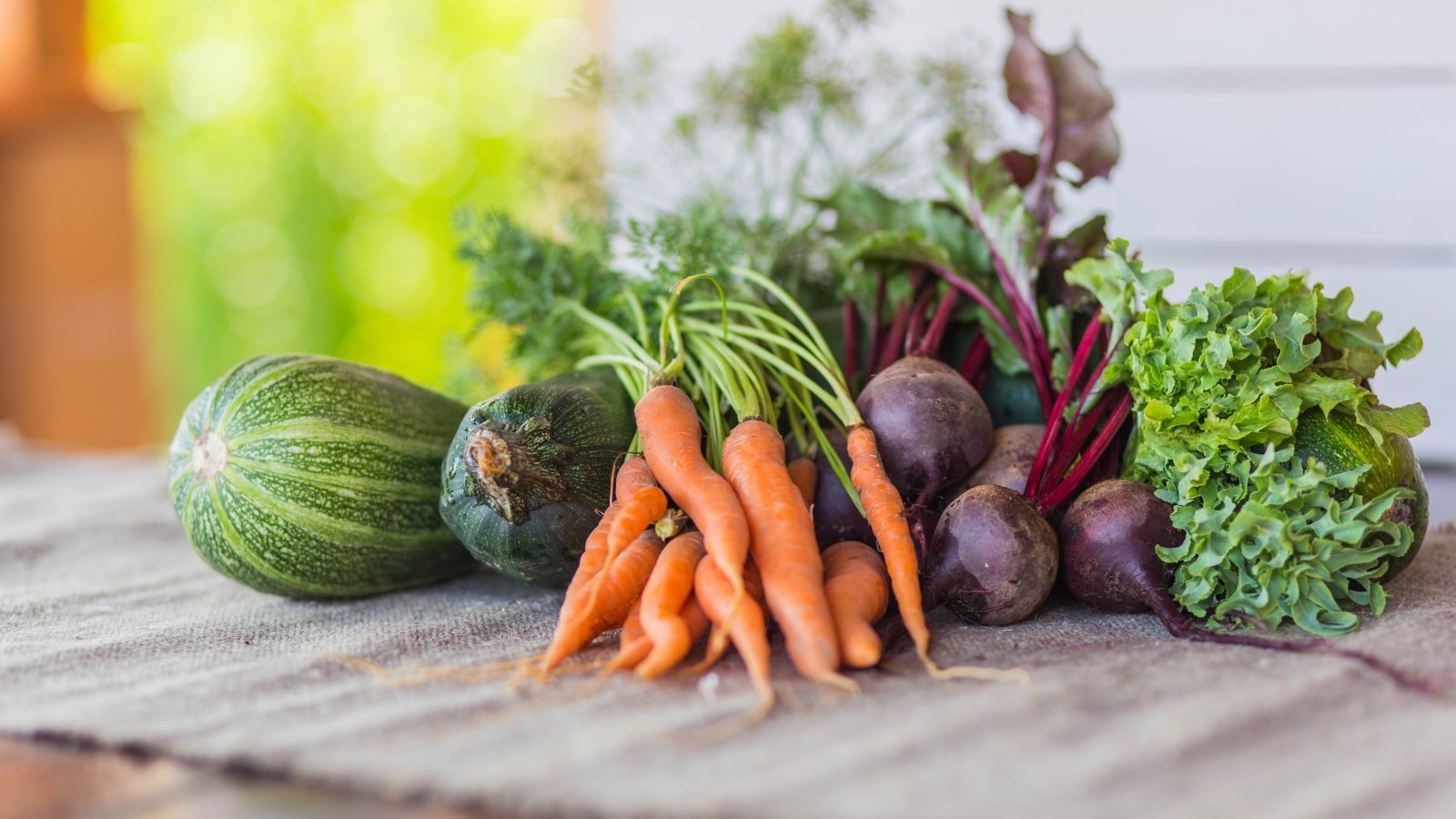 Carrots, zucchini, and beets placed on a wooden table.
