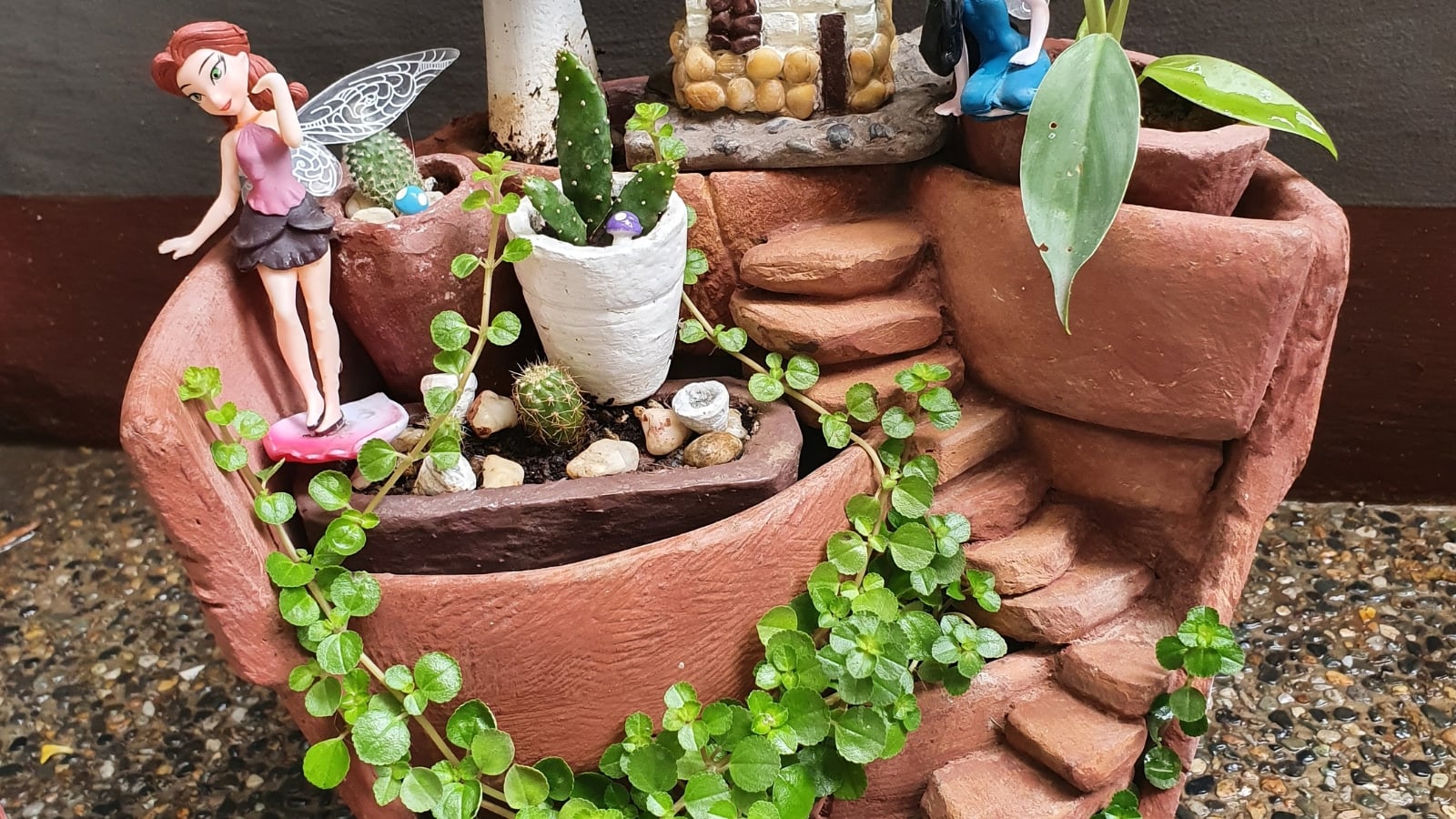 A ceramic container with Lysimachia nummularia, displaying trailing green leaves, paired with succulents and miniature figurines.