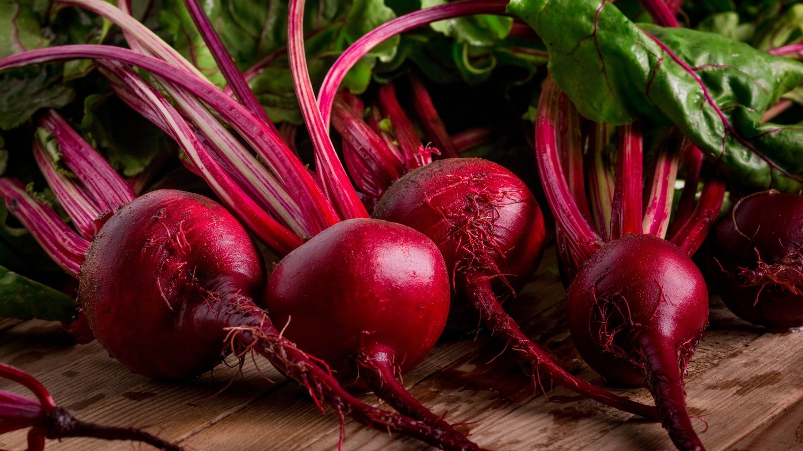 A group of vibrant red beets on a wooden table.