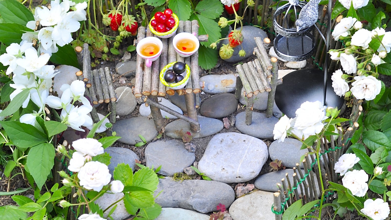 Rosa 'Snow Bride' with white flowers and green foliage surrounding a small stone pathway with tiny lanterns.