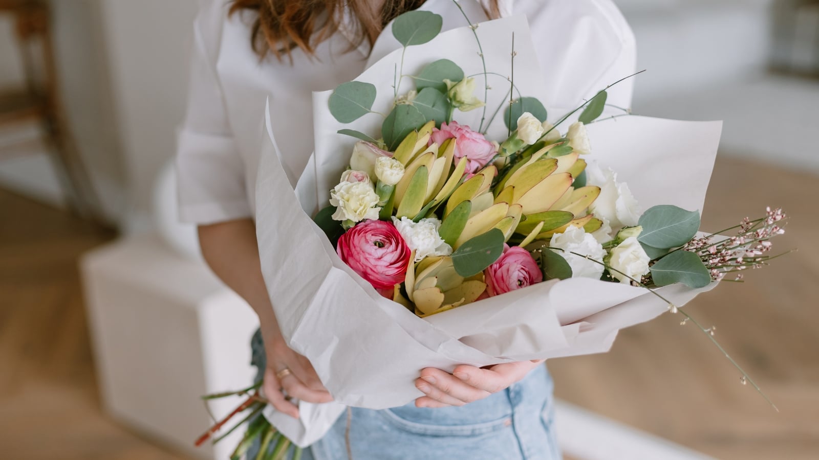 Person holding a bundle of freshly cut Inch Plants, roses, and daisies wrapped in white paper.
