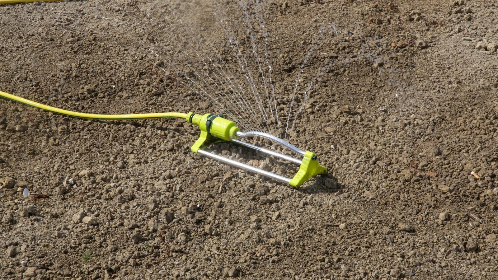 Yellow soil moisture meter stuck in dry, compacted brown soil, displaying moisture levels on its dial.