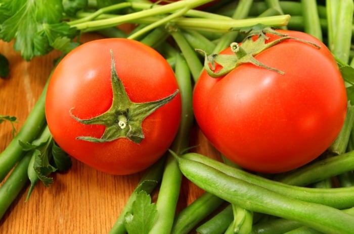A close-up shot of several red fruits and greed legume pods that showcases plant tomatoes with green beans