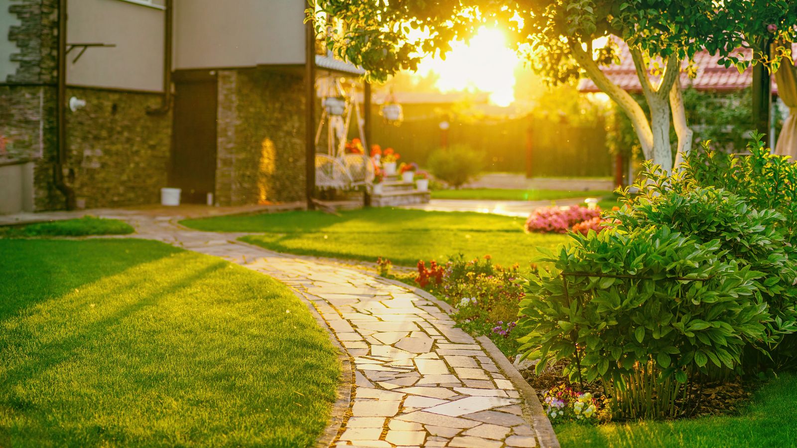 A shot of a yard area featuring a pathway and various plants and flowers on a grassy area outdoors