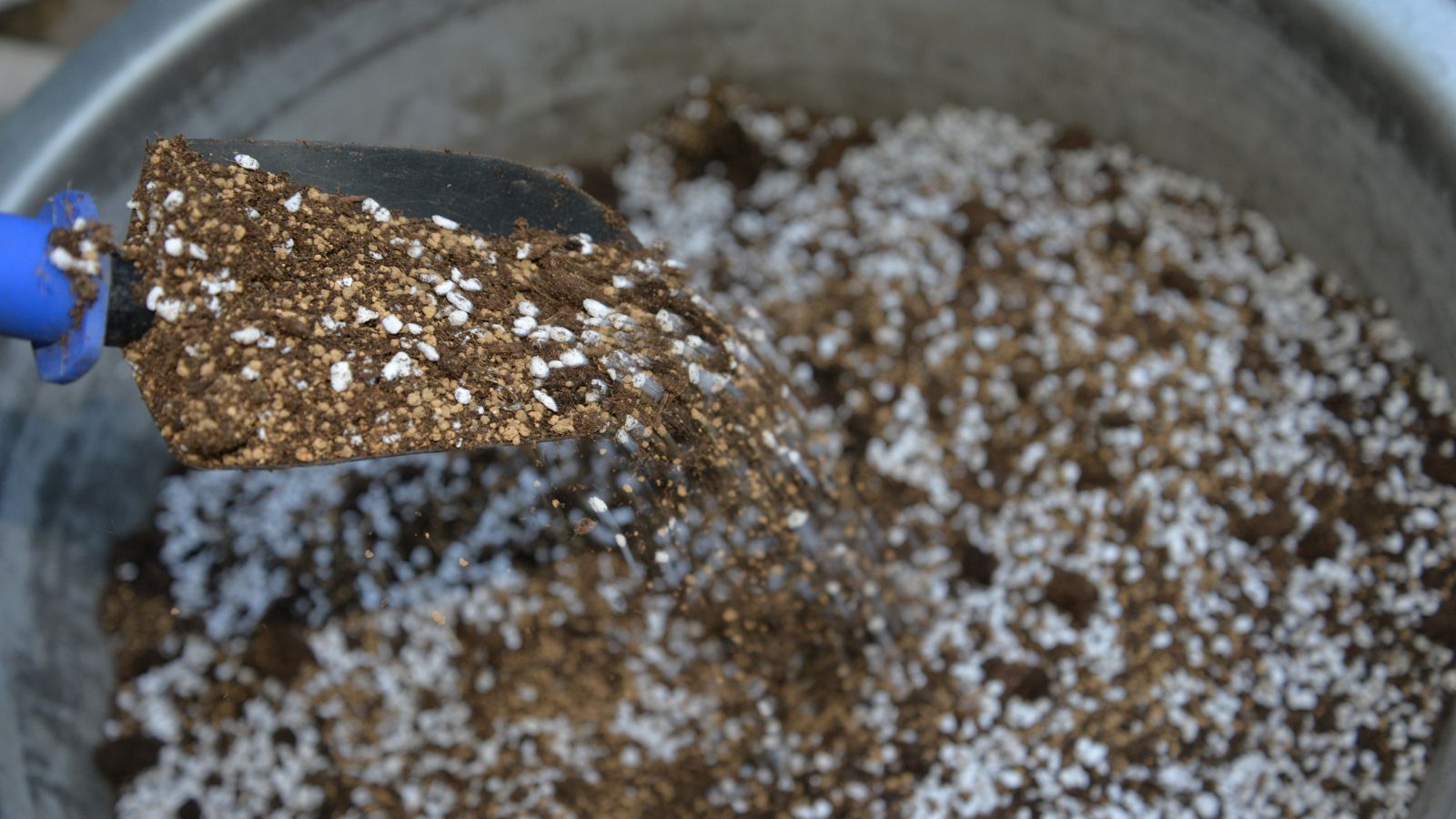 An overhead shot of a hand trowel with a potting mix on a container all situated in a well lit area indoors