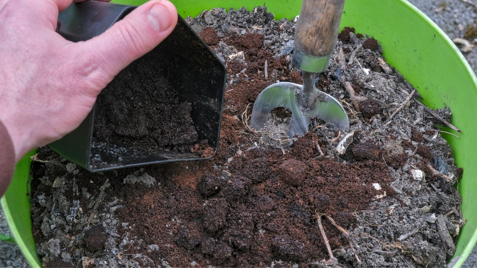 A close-up shot of a person adding sediments on soil and other debris on a green colored pot outdoors