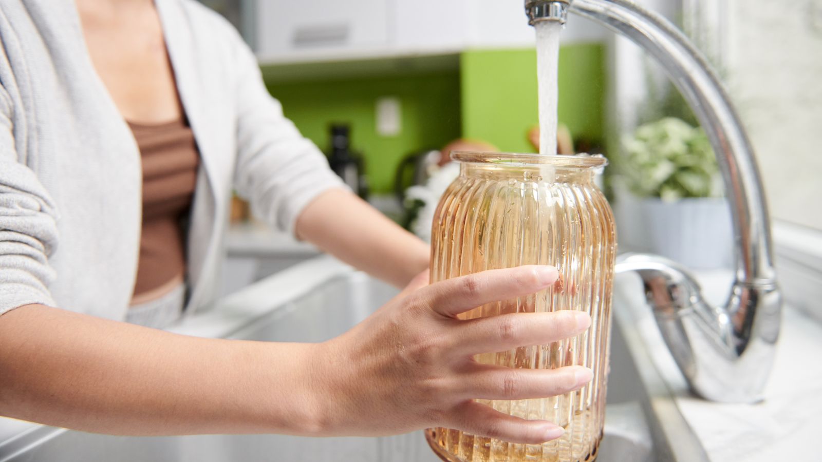 A close-up shot of a person holding a glass container, in the process of filling it with clean water indoors