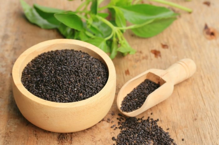 A close-up shot of a wooden container filled with freshly harvested black harvest germs of an herb, showcasing how to save basil seeds