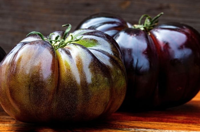 A close-up shot of several freshly harvested fruits, showcasing black purple tomato varieties