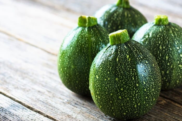 A close-up shot of several round fruits of a summer squash variety, showcasing heirloom zucchini varieties