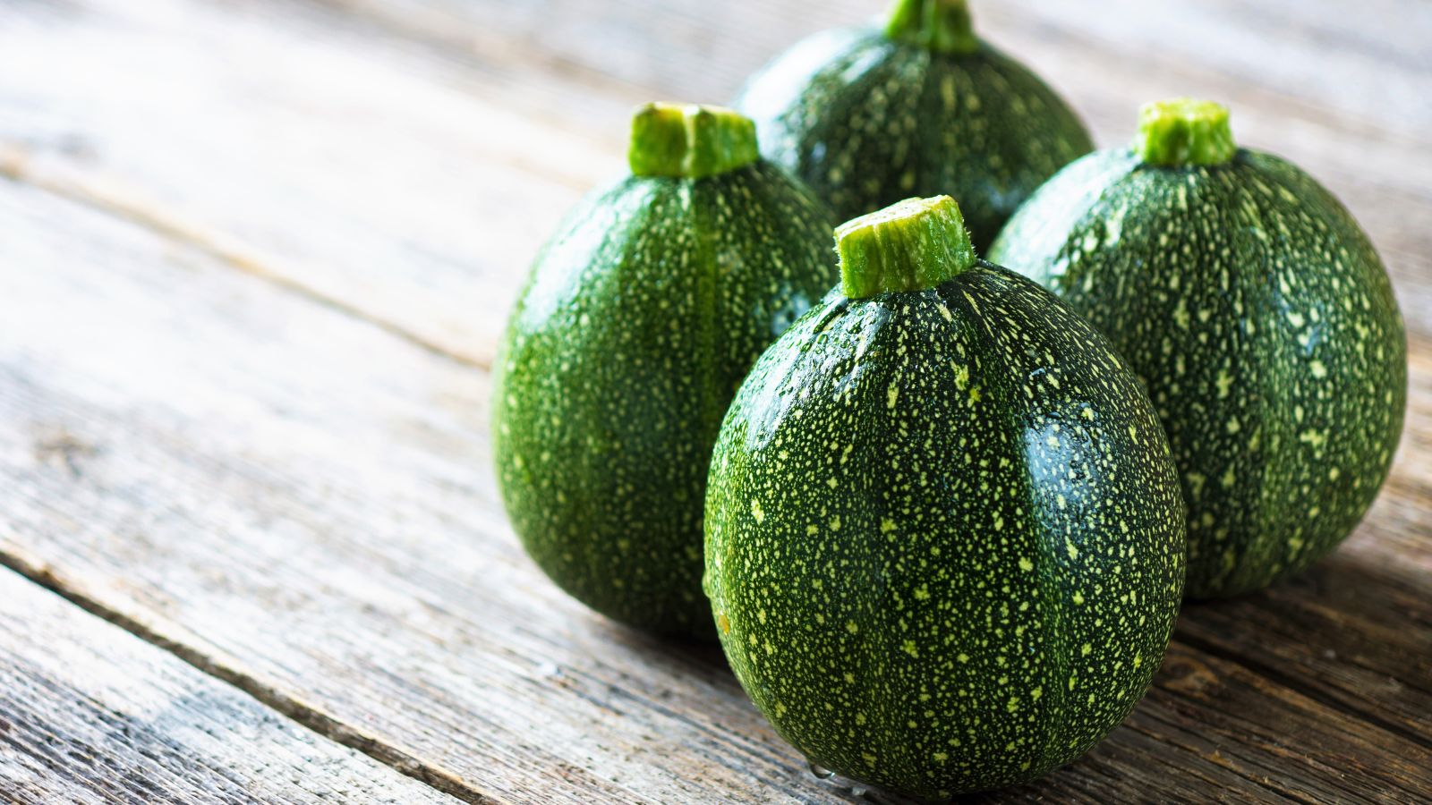 A close-up shot of several round fruits of a summer squash variety, placed on top of a wooden surface