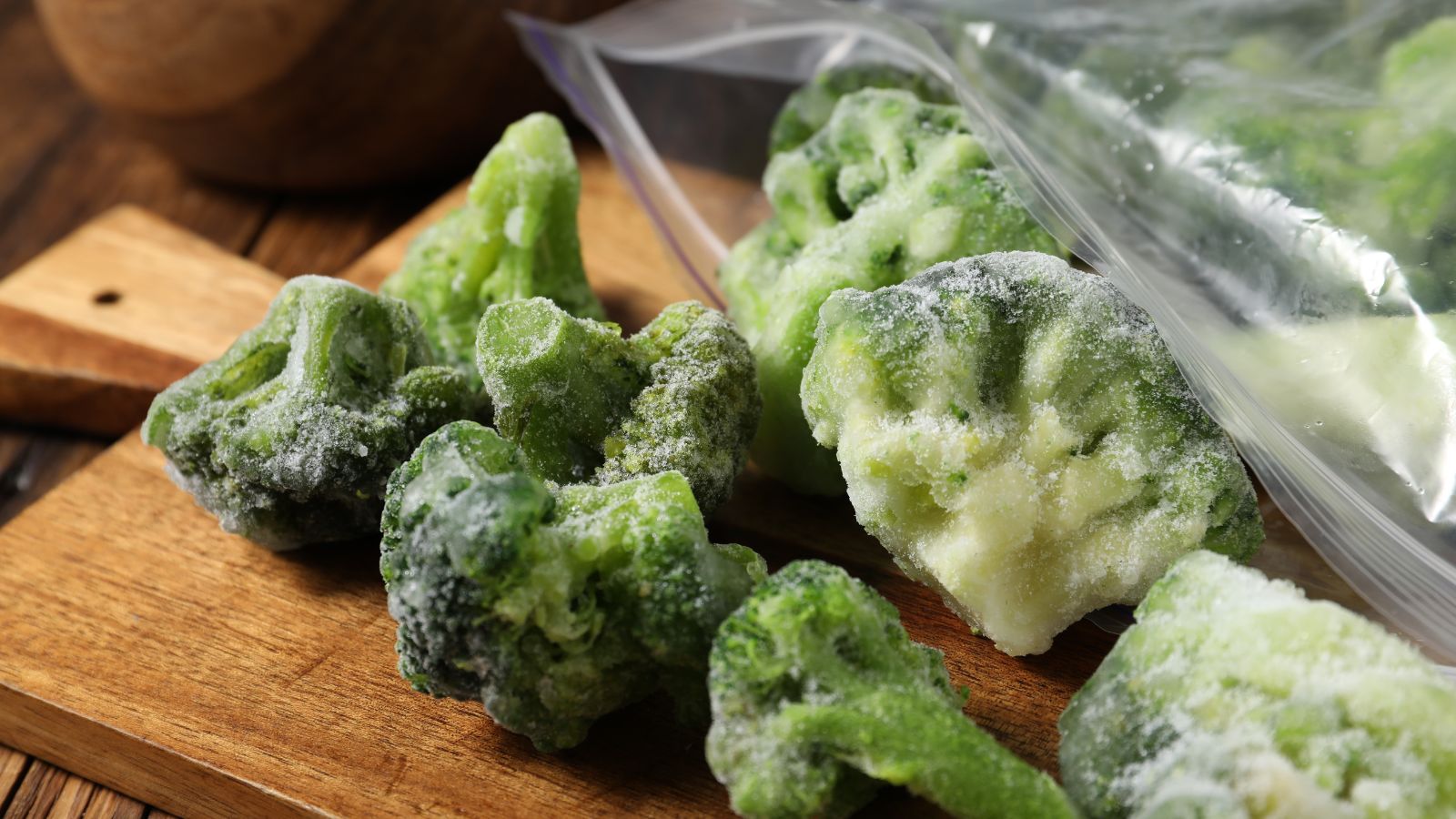 A close-up shot of several small frozen heads of a crop placed on top of a wooden copping board and a plastic ziplock bag
