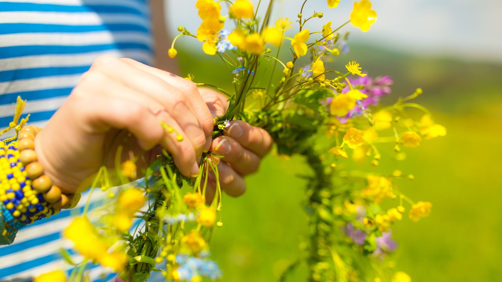 A person using bundles of blooms to create a crown, made using small yellow blooms