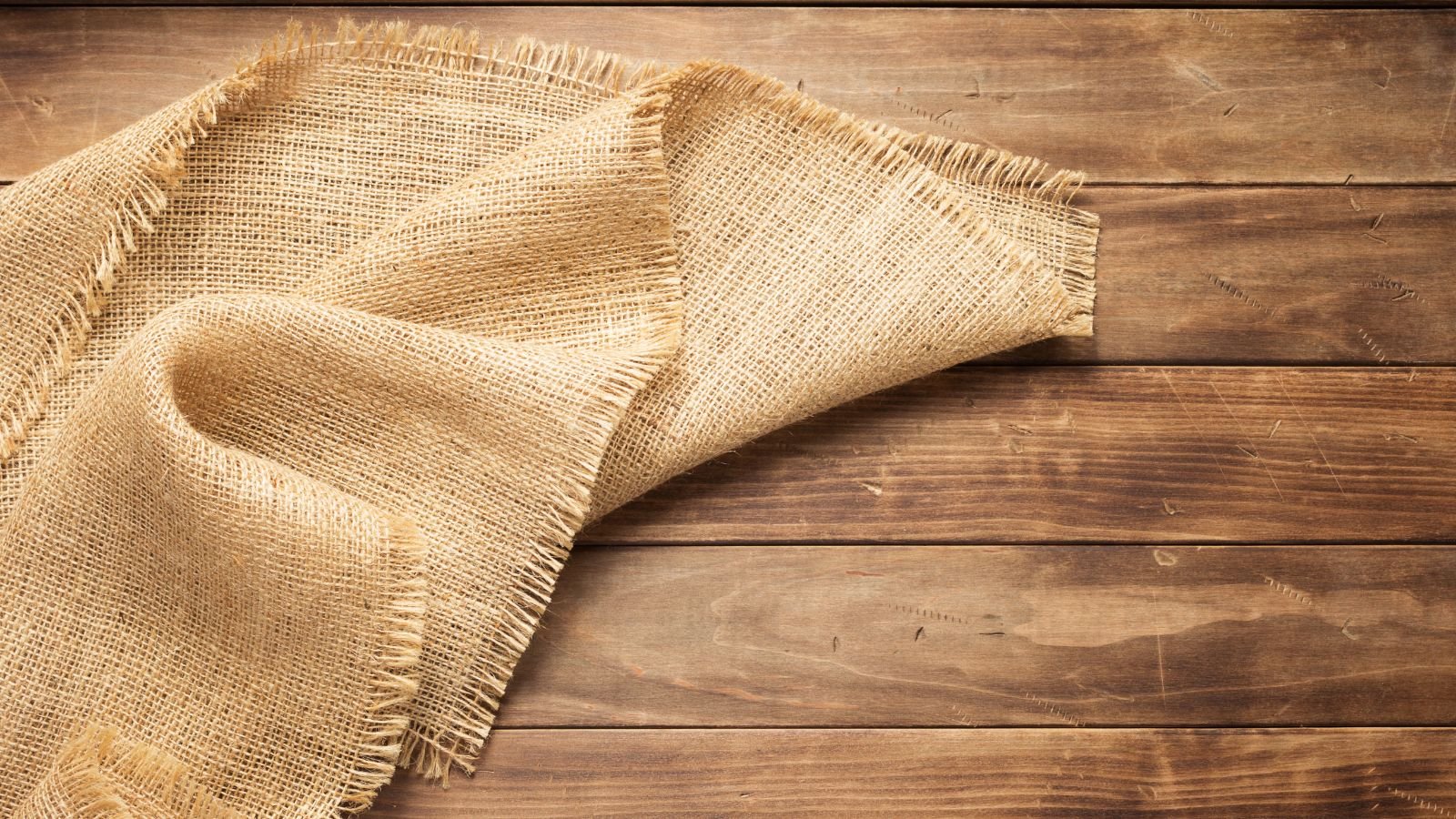 A sheet of burlap with folds placed on top of a wooden surface, located somewhere with sunlight