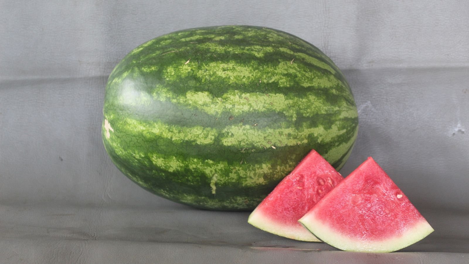 A shot of a large freshly harvested fruit alongside several slices of the fruit placed in a well lit area indoors