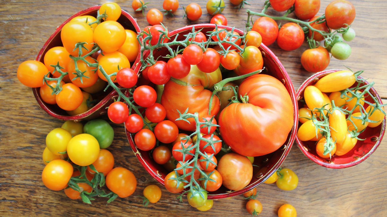 An overhead shot of several freshly harvested fruits on different bowls on a wooden surface indoors