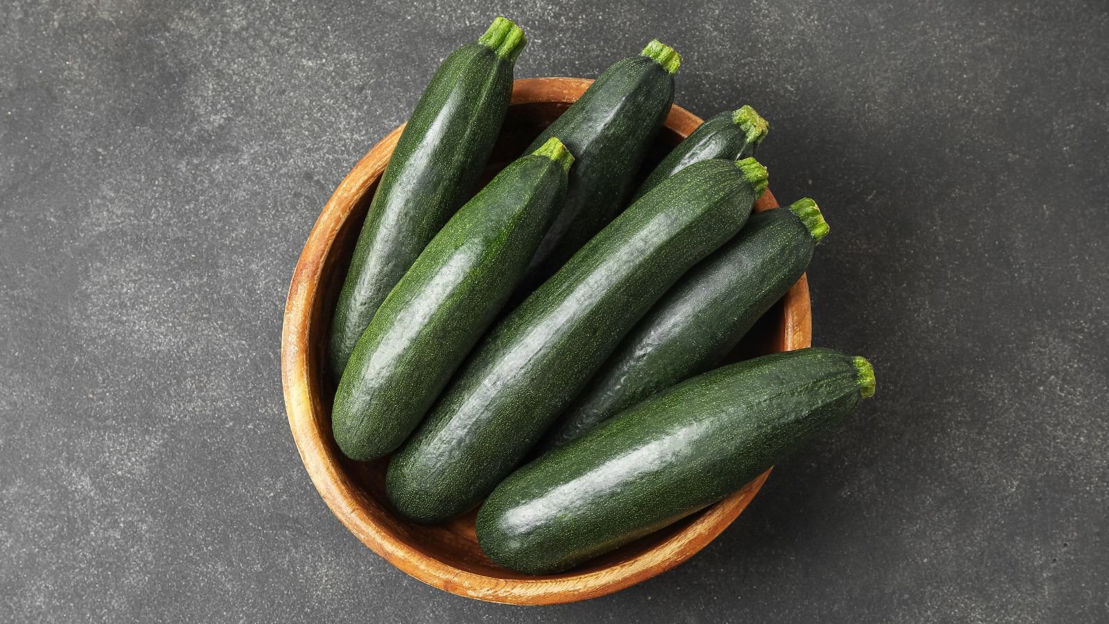 An overhead shot of several freshly harvested, compact fruits with dark-green color of the Cucurbita pepo ‘Nero di Milano’ variety, all placed in a bowl indoors
