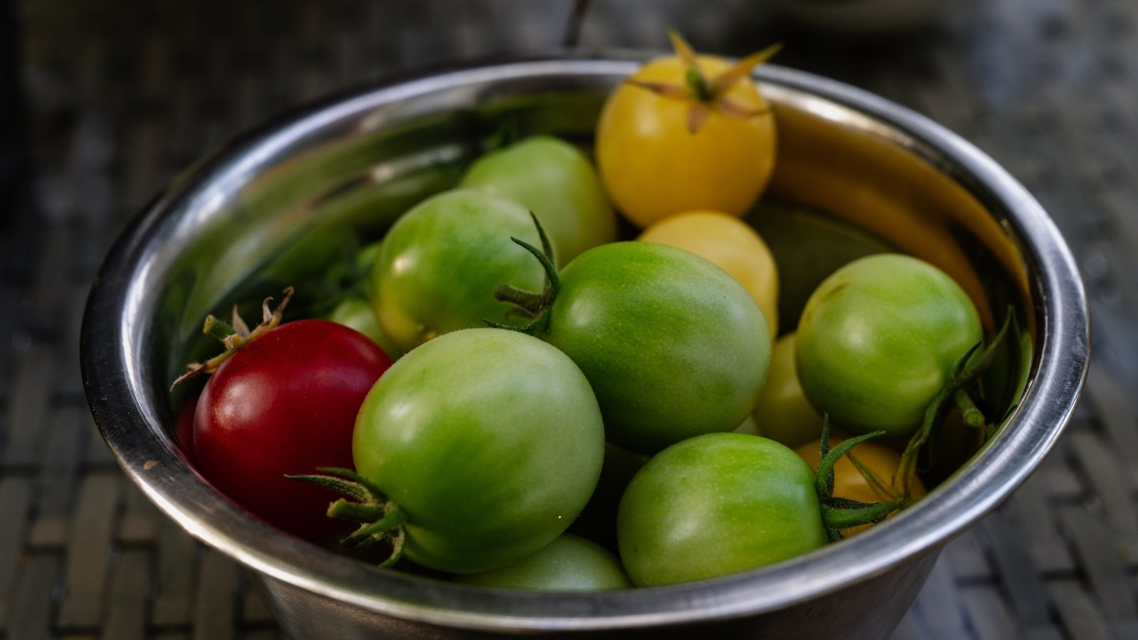 Close-up of a bowl full of unripe green tomatoes, oval shaped, with glossy thin skins, on a kitchen countertop.