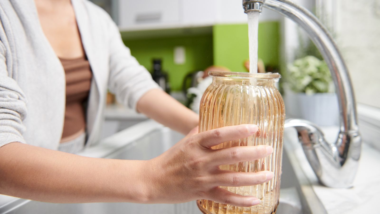 A close-up shot of a person in the process of refilling a glass vase with fresh and clean water indoors