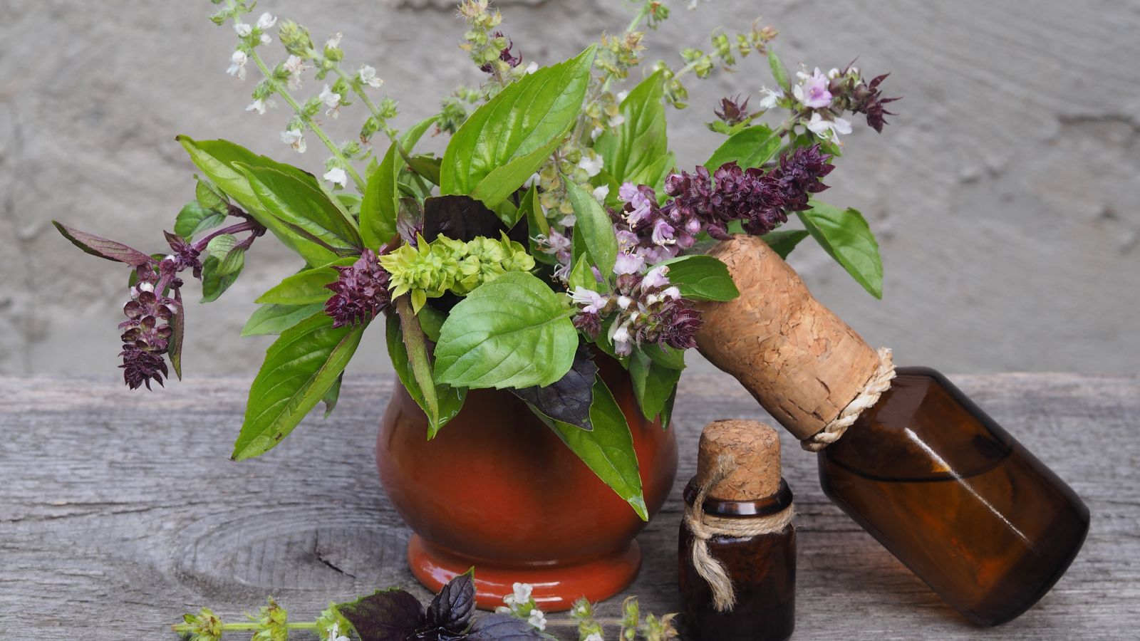 A close-up shot of a vase filled with blooming herbs alongside small vials on a wooden surface indoors