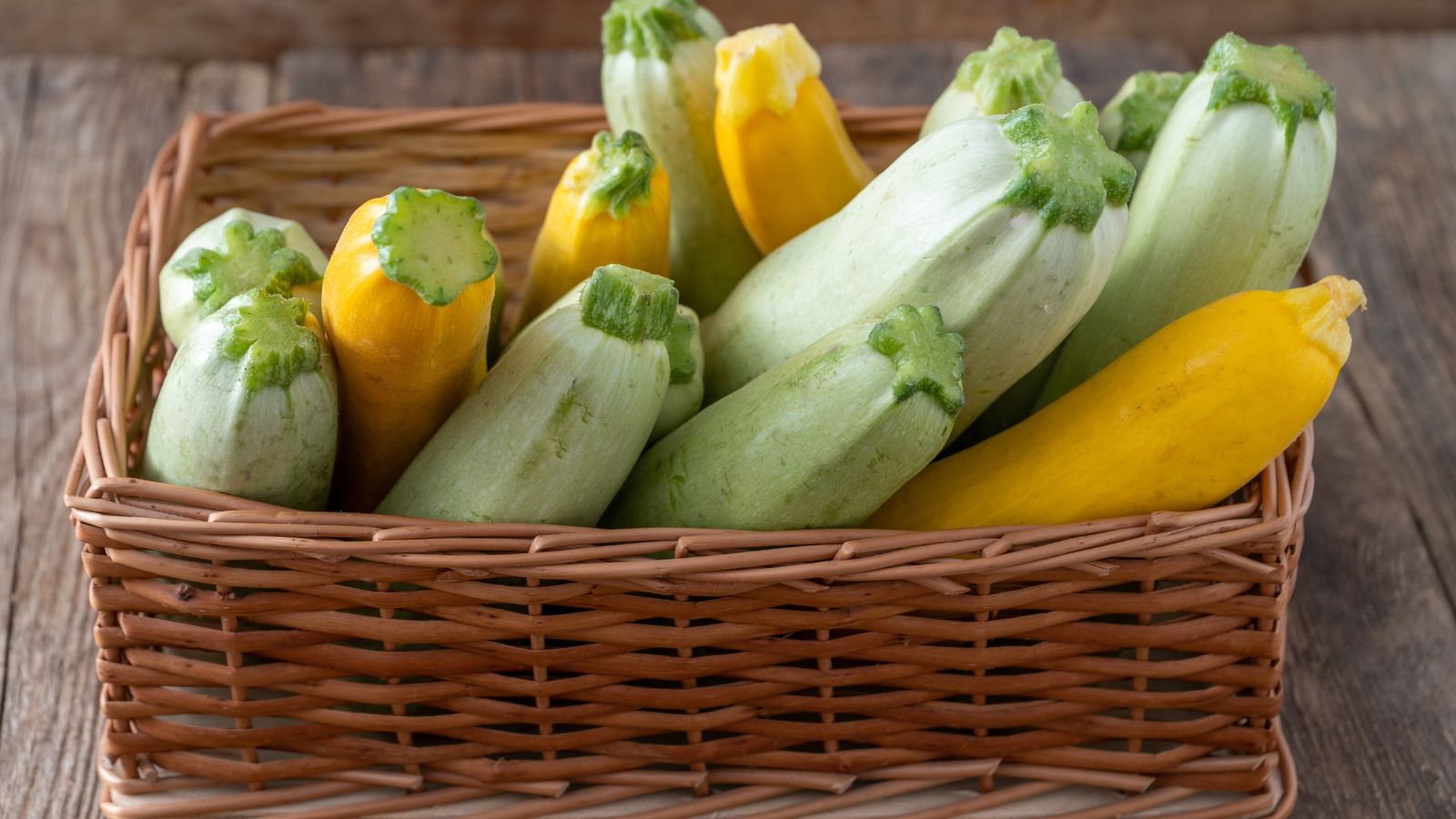A shot of a rectangular wicker basket filled with several freshly collected fruits placed on a wooden surface indoors