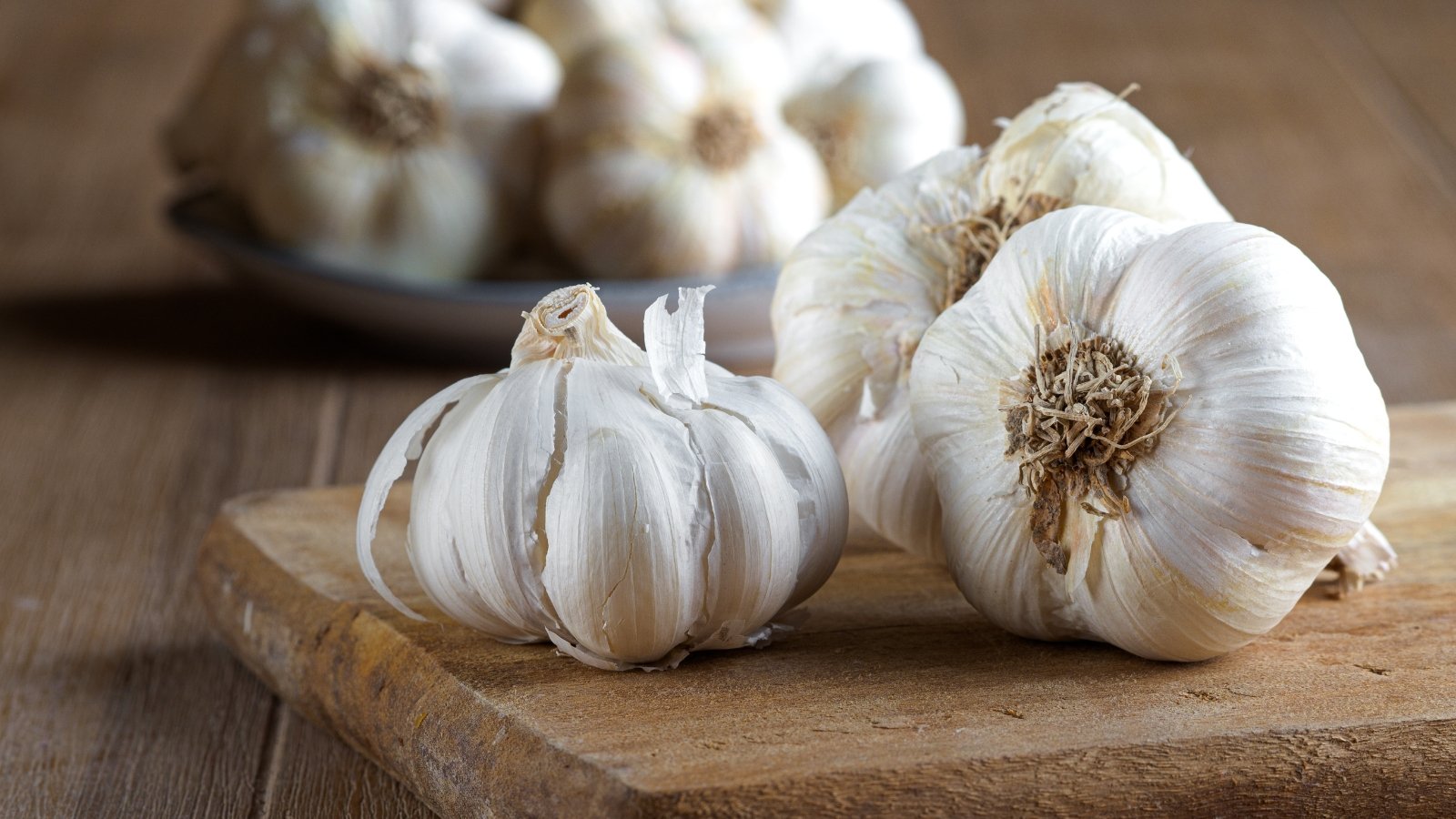 Smooth, silvery-white skins cover tightly packed cloves in rounded, uniform bulbs on a wooden surface.