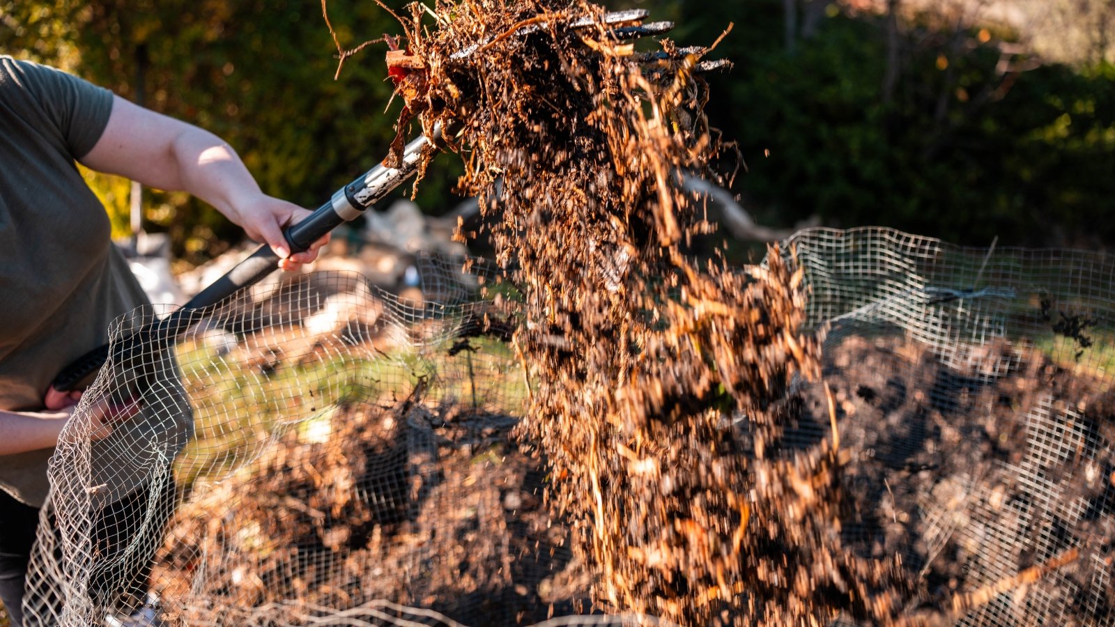 A female gardener with a large shovel turns a compost pile to improve air ventilation.