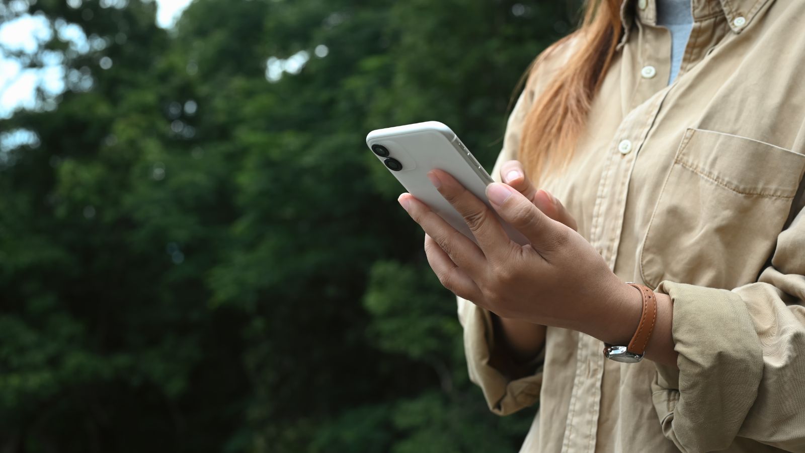 A shot of a person in the process of using their phone in a garden area outdoors