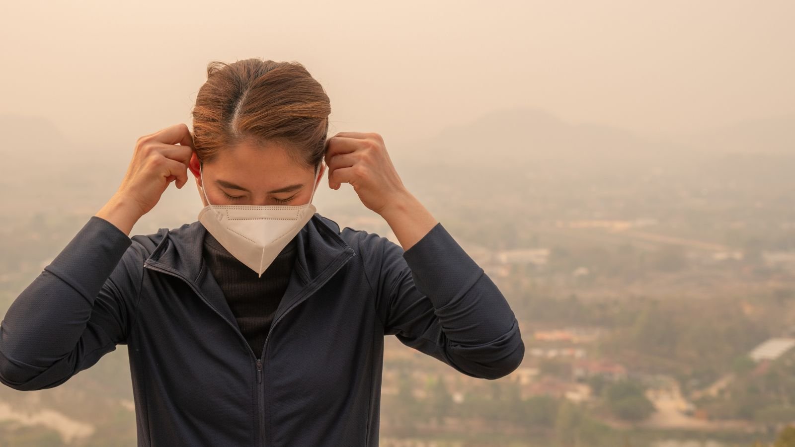 A close-up shot of a person wearing a jacket and a face mask situated in a fume covered area outdoors