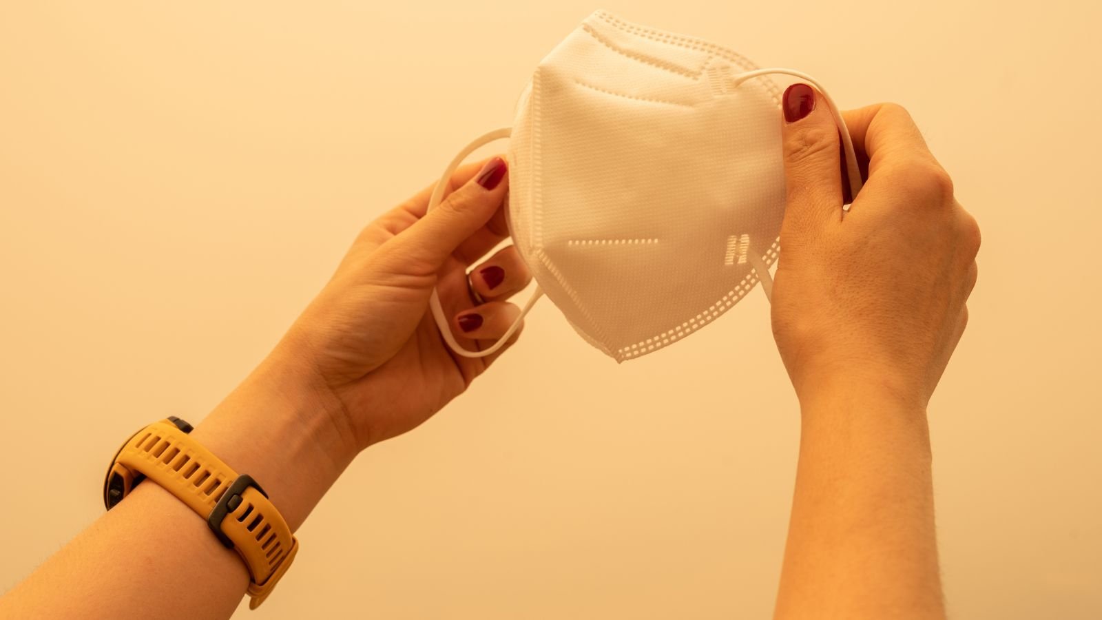 A close-up shot of a person's hand holding a facemask in an area covered in fumes