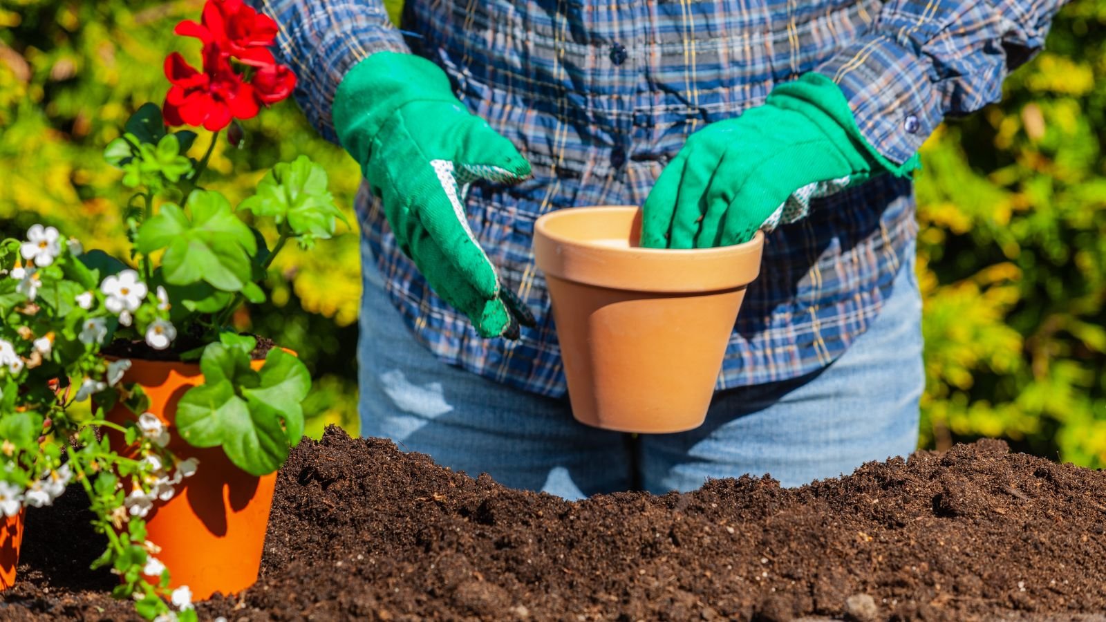 A gardener wearing bluegreen gloves while holding a clay pot with a pile of soil under it
