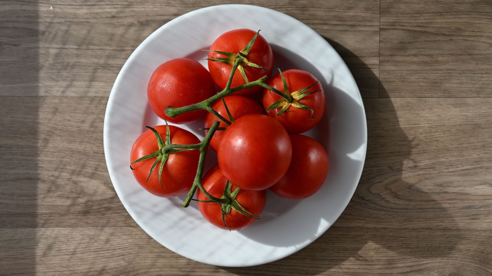 An overhead shot of a small composition of picked fruits, still ripening on their vine, placed on a white plate on a wooden surface indoors