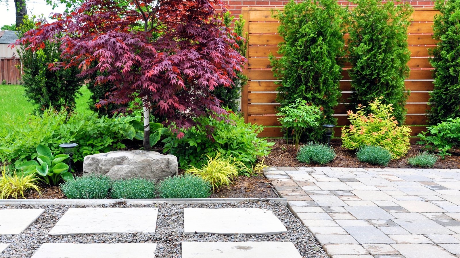 A modern Asian-inspired Japanese garden with a tumbled paver patio, flagstone walkway, and horizontal cedar fence framed by minimalist greenery in an urban backyard.