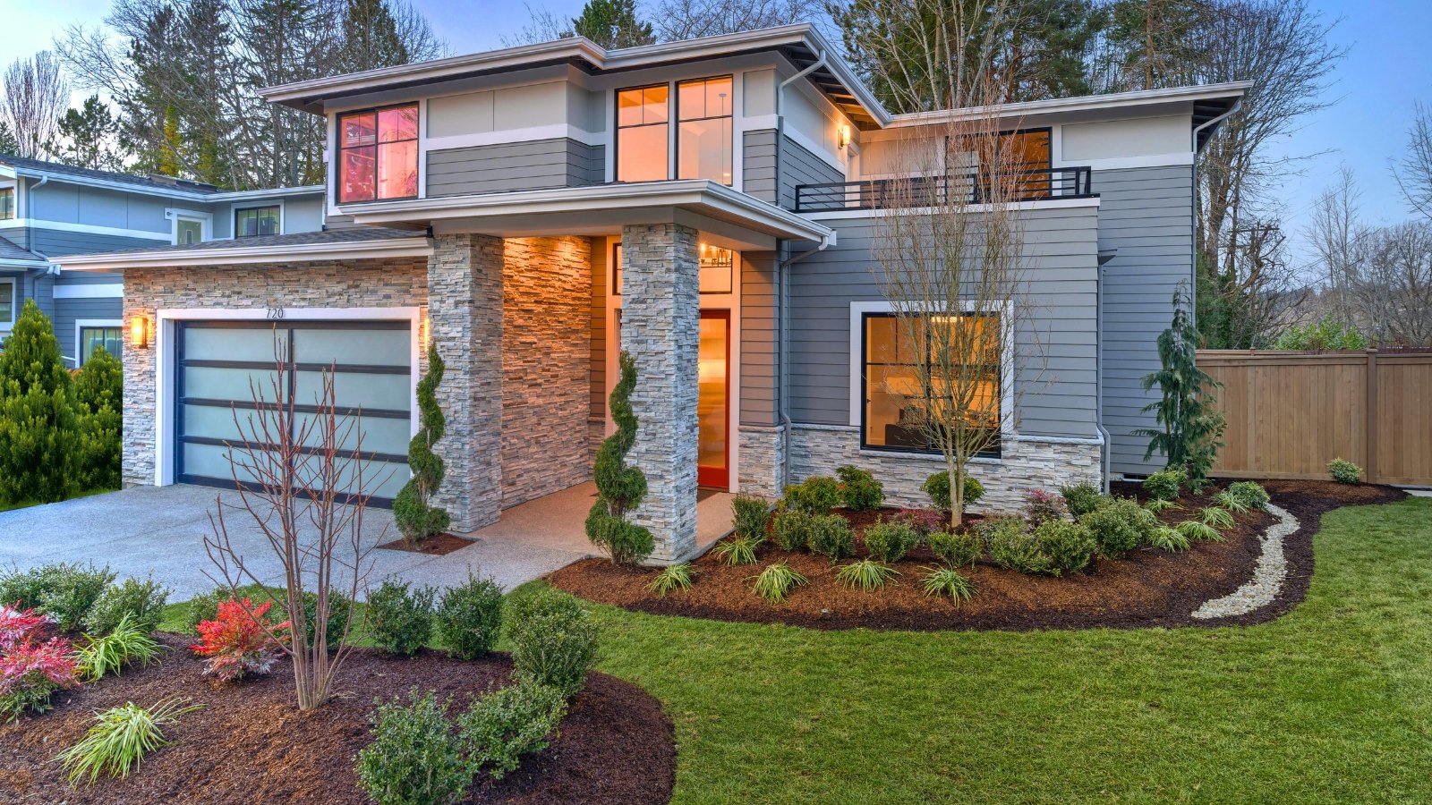 Modern contemporary house with stylish landscape including mulched flowerbeds with evergreen bushes, ornamental grasses, bare trees and topiary.