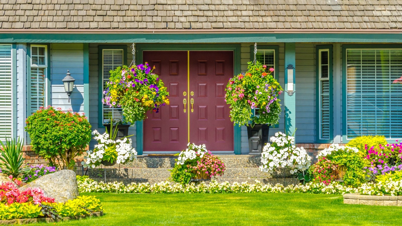 Beautifully landscaped front yard with blooming flower beds and hanging containers of colorful flower arrangements dangling in front of the home's entrance.