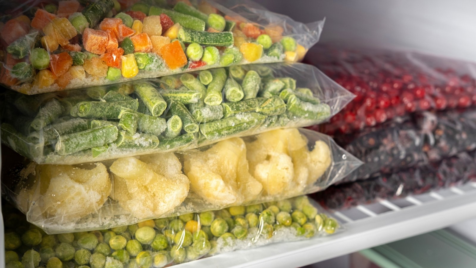 Plastic bags filled with various frozen vegetables stacked neatly inside a freezer.