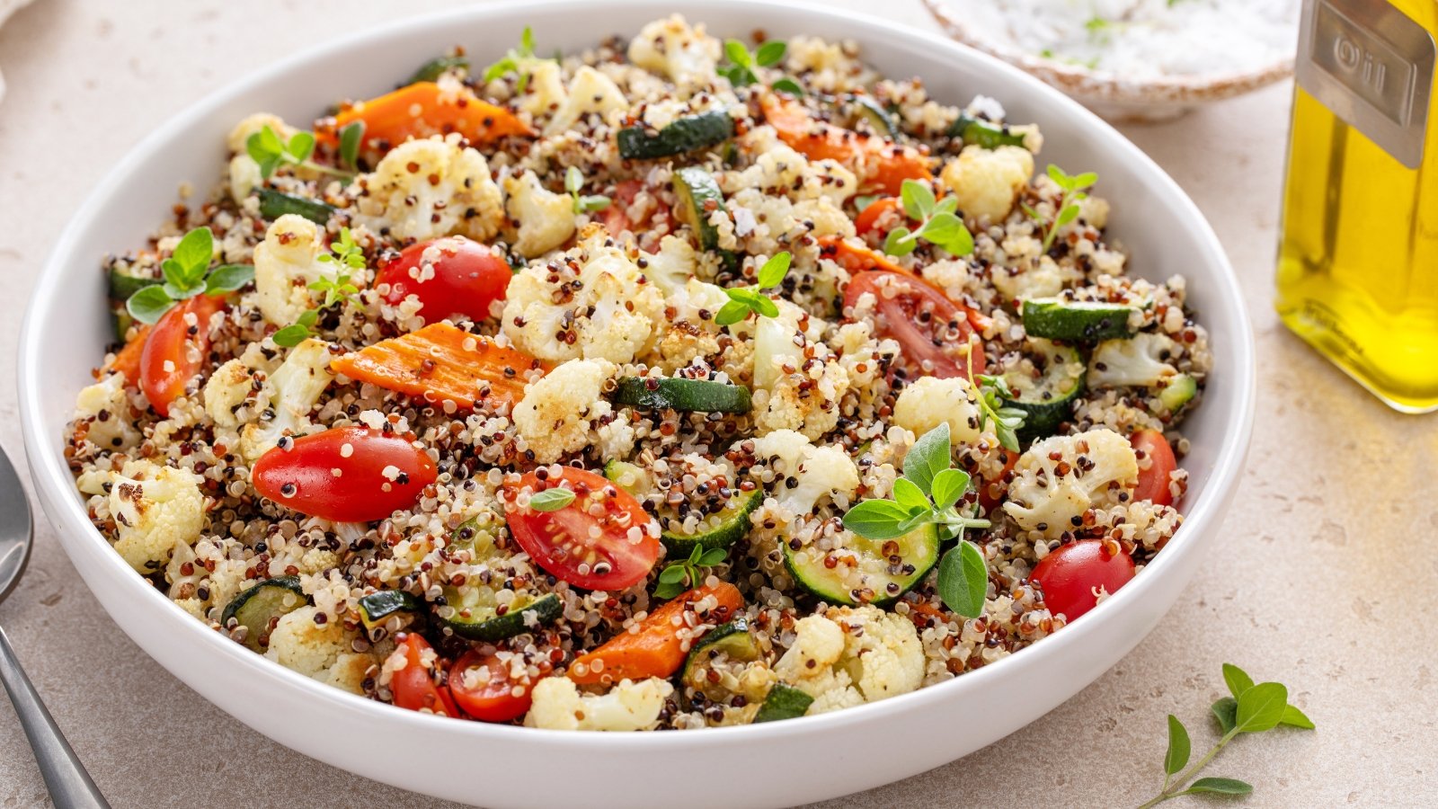 Close-up of quinoa salad with roasted vegetables, cauliflower and zucchini, and fresh herbs and tomatoes in a large white plate.