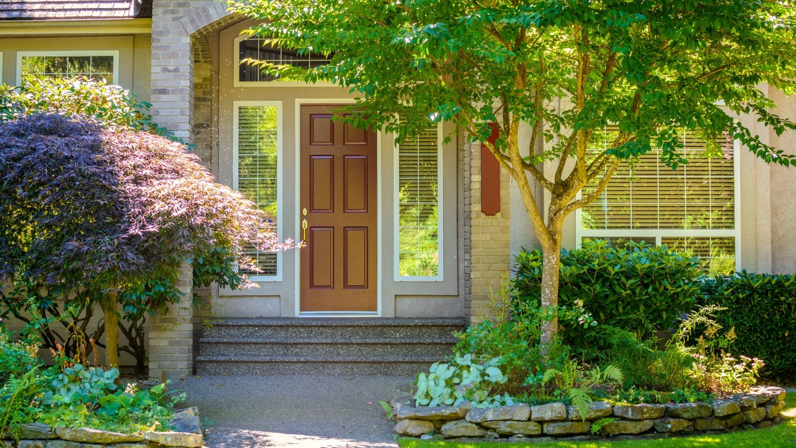The small garden in front of the house's entrance consists of several trees with purple and green foliage, boxwood bushes and shade-loving perennials.