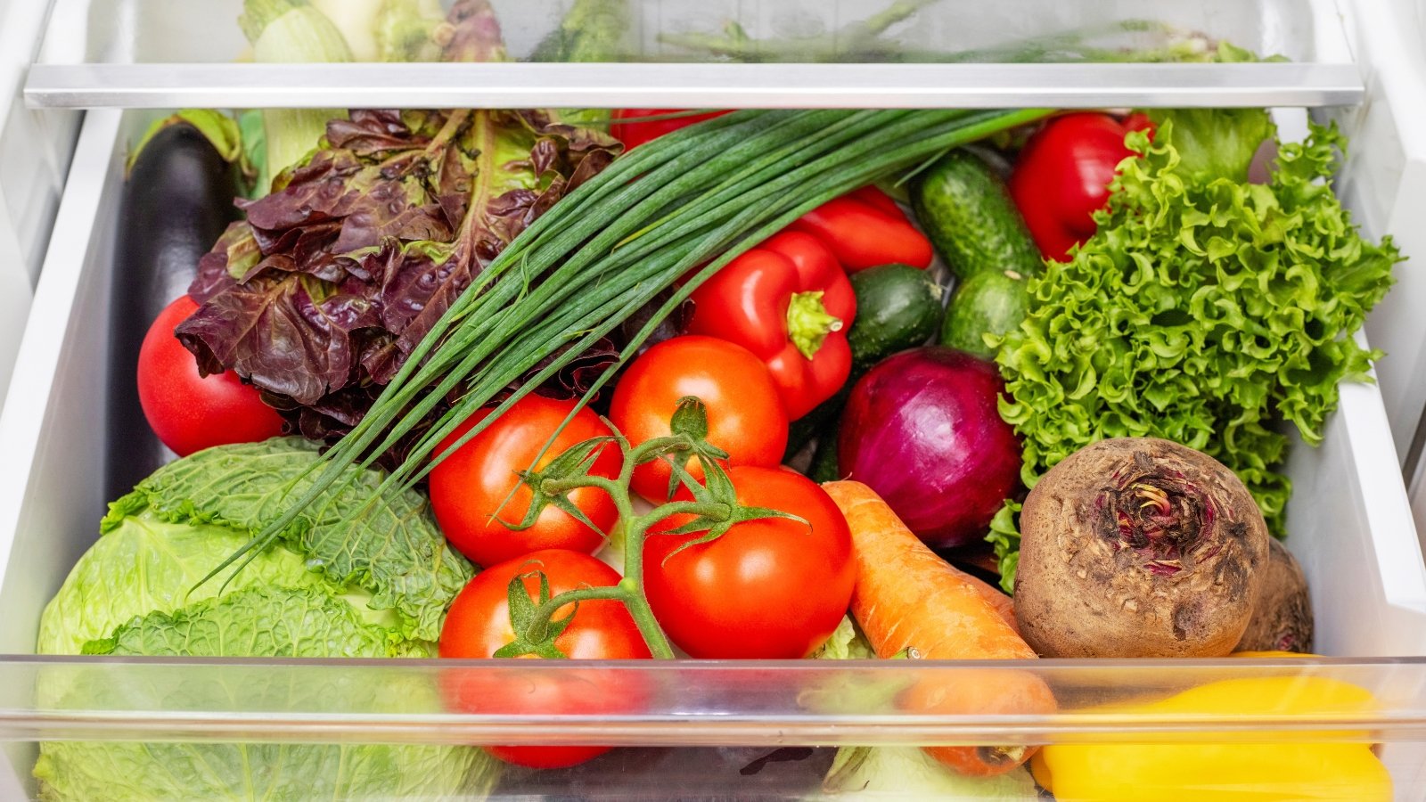 The refrigerator drawer is completely filled with fresh vegetables, including beets, tomatoes, cabbage, carrots, eggplant, onions, cucumbers, peppers and others.