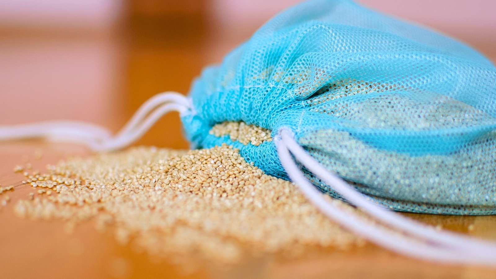 Small, round, white quinoa seeds in a clear blue reusable bag on a wooden table.