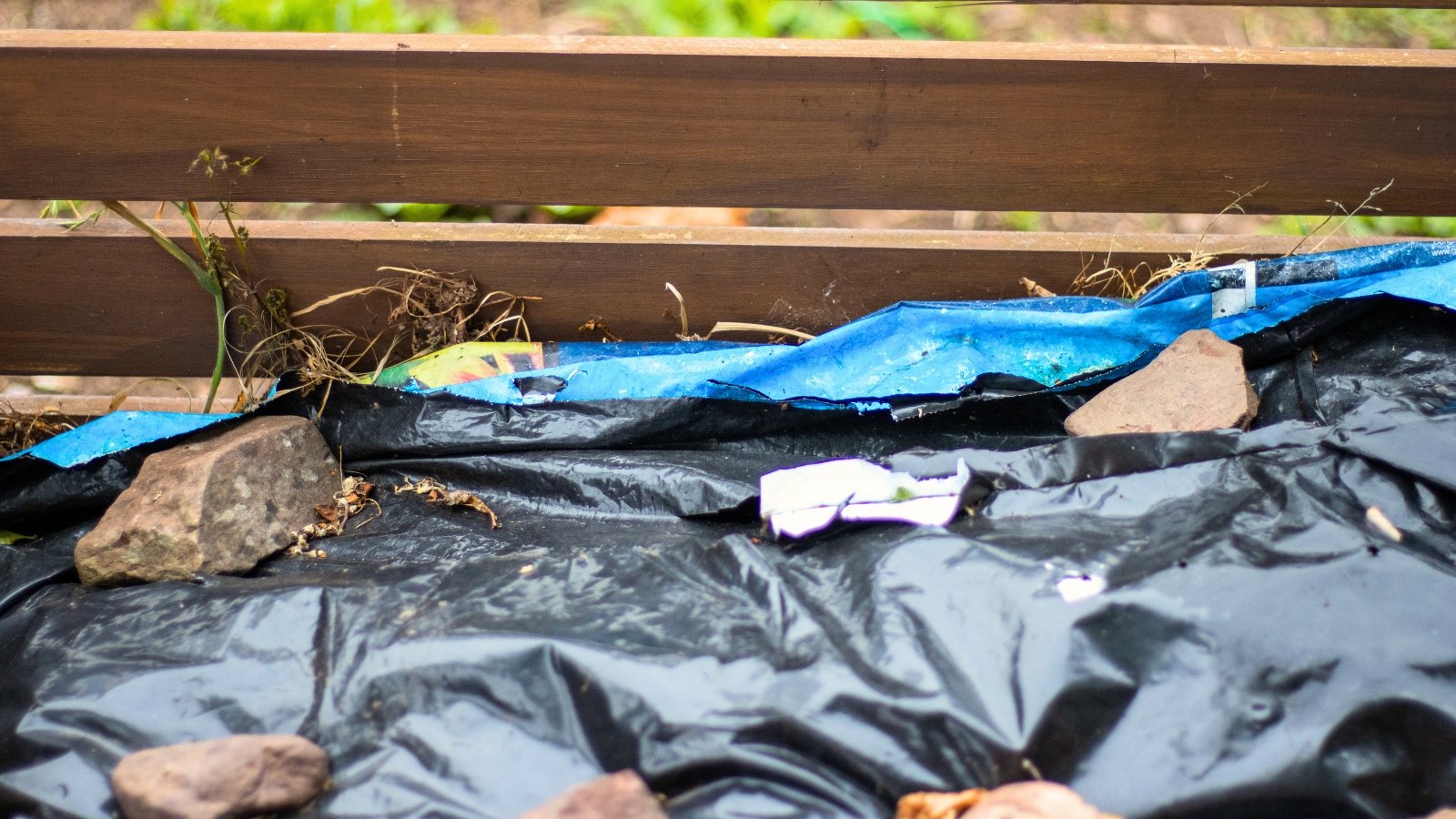 Close-up of a wooden compost bin covered with black plastic top cover.