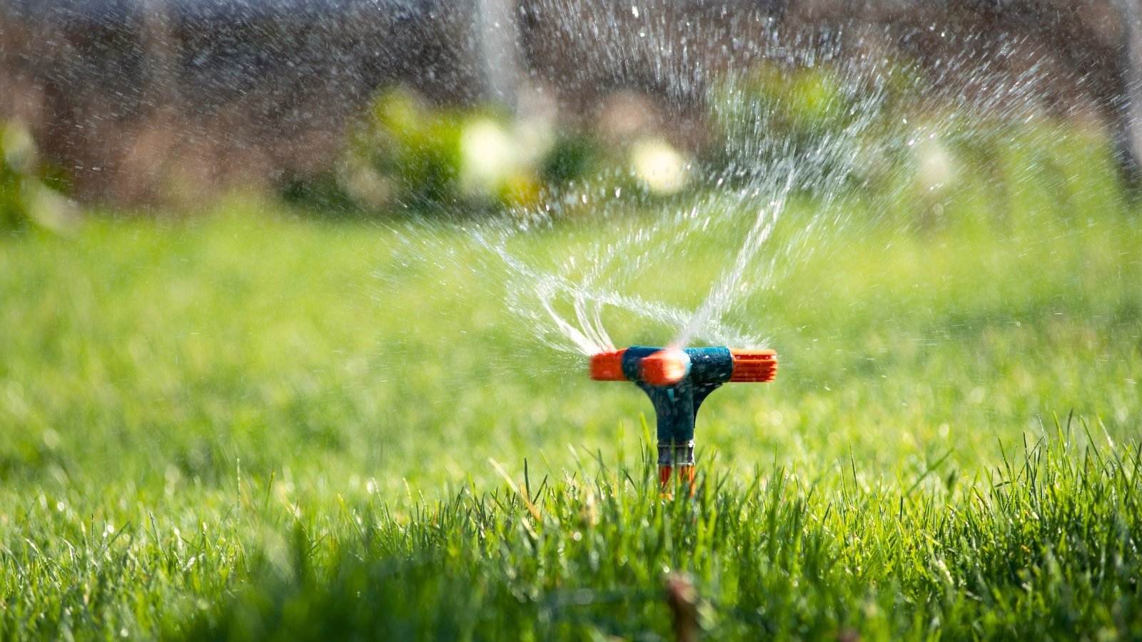 Close-up of a sprinkler spraying water in a circular motion, creating fine droplets that evenly cover a green lawn in the garden.