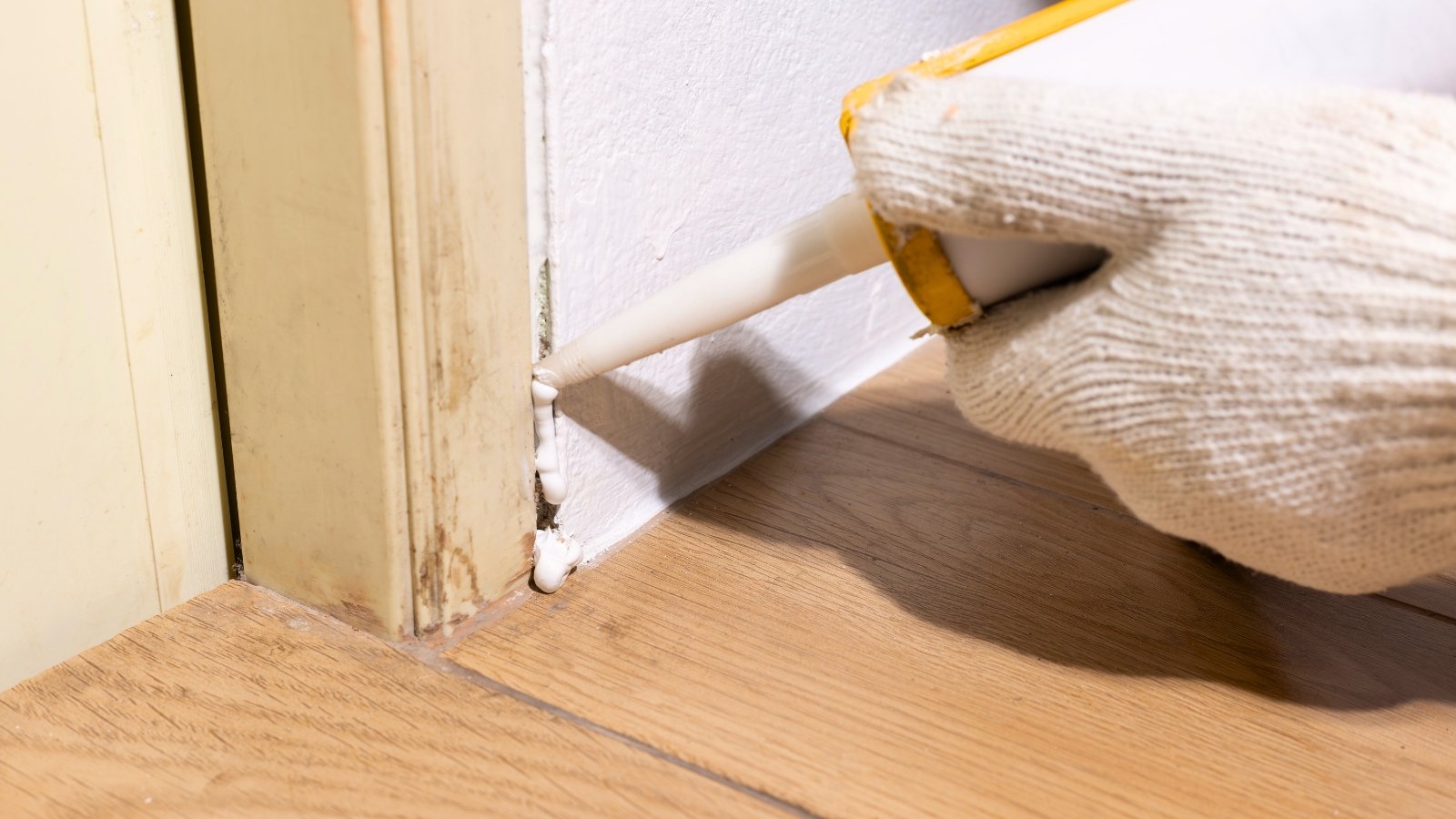 A handyman applies acrylic sealant to a rotten door frame base to block ants from entering a room.