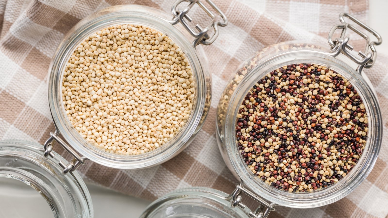 Top view of multicolored quinoa seeds in two glass jars with lids standing on a checkered napkin.